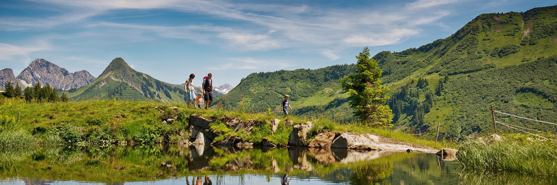 Familie mit kleinen Kindern vor einem Teich beim Wandern in den Bergen im Sommer