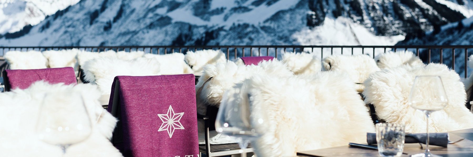 Tische und fellbedeckte Stühle des Restaurants Alpenstern mit Blick auf die verschneiten Berge
