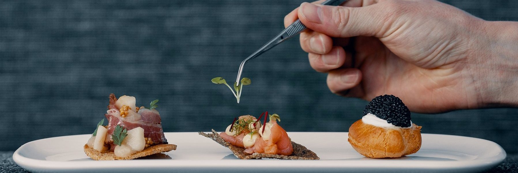 Gericht mit Speck, Lachs und Kaviar wird mit einer Küchenzange dekoriert
