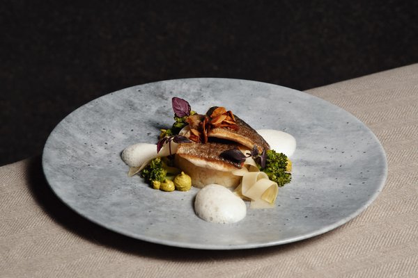 Liebevoll dekoriertes Gericht mit Fisch und Gemüse auf einem grauen Teller