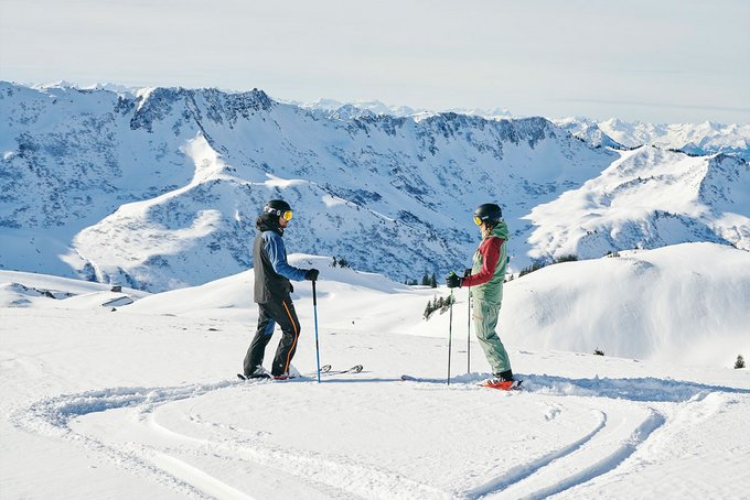 Frau und Mann beim Skifahren in den Alpen bei Sonnenschein mit Blick auf die verschneiten Berge
