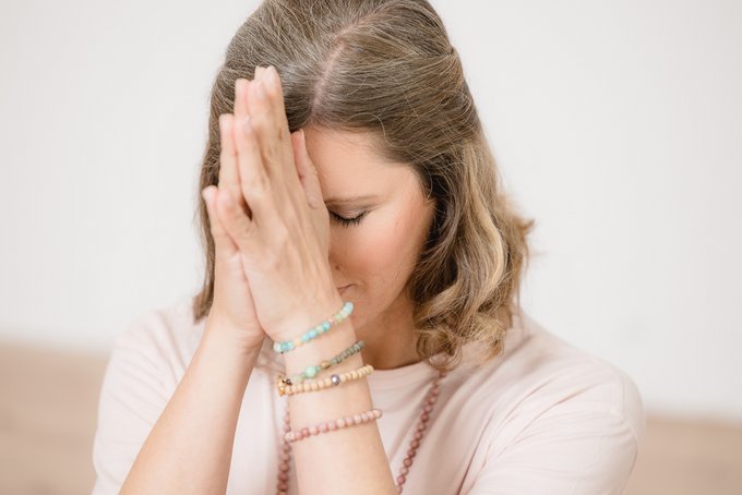 Frau mit geschlossenen Augen und bunten Armbändern meditiert mit gefalteten Händen