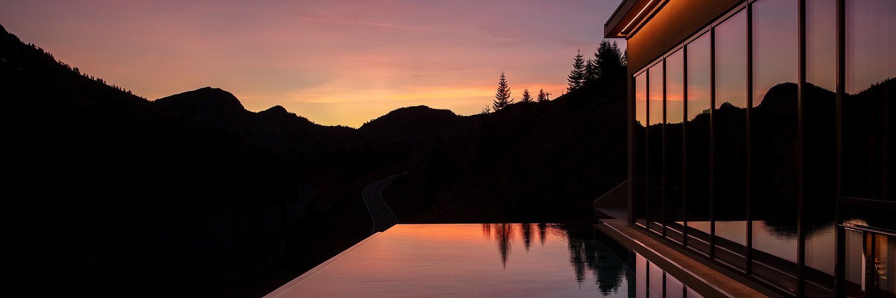 Spiegelnder Outdoor Infinity Pool vor einer Bergsilhouette bei Dämmerung