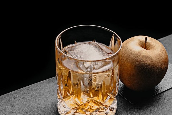 Cocktail mit Eis in einem Lowball Cocktail Glas und einem goldenen Apfel