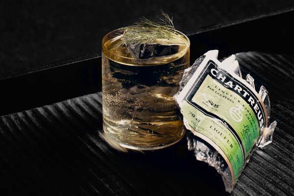 Cocktail auf Eis mit Dill und eine kaputte Flasche Chartreuse