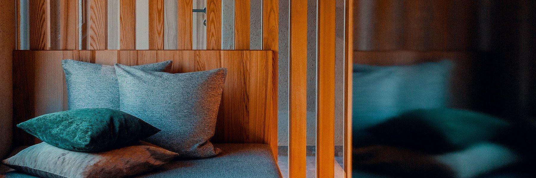 Liegesofa mit Kuschelkissen und moderner Deckenlampe vor einem Trennelement aus Holz