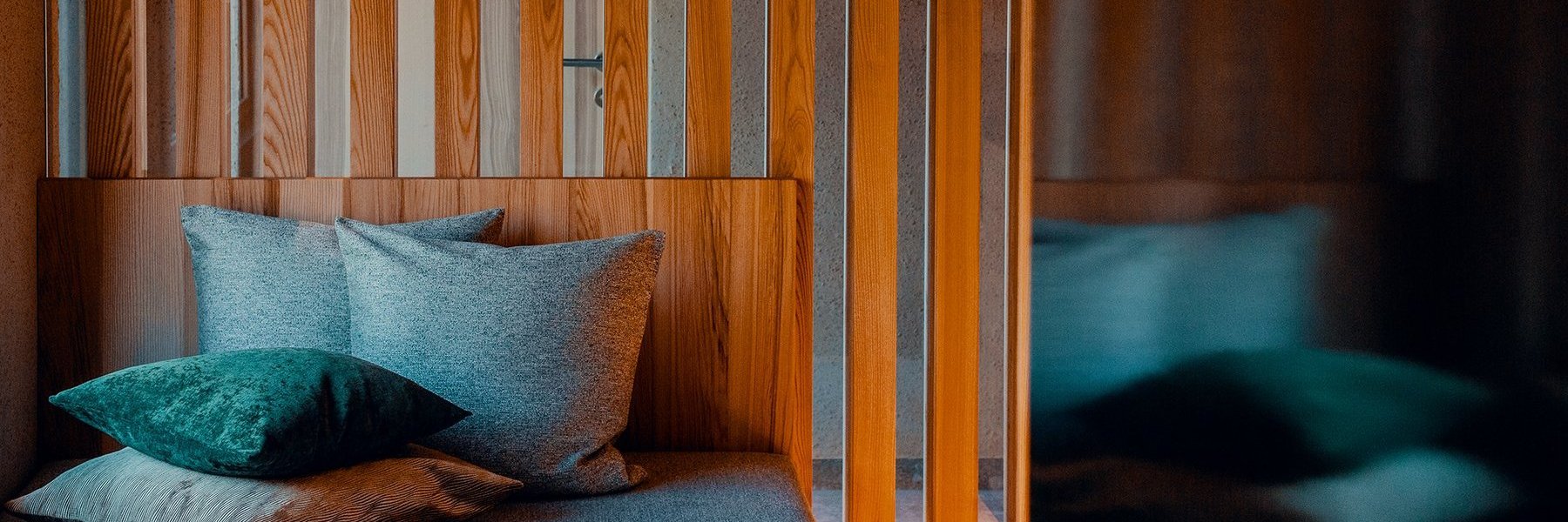 Liegesofa mit Kuschelkissen und moderner Deckenlampe vor einem Trennelement aus Holz